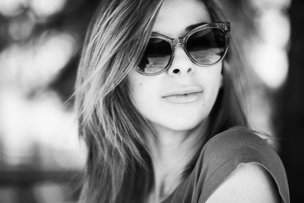 Güneş gözlüğü takan, gündüz vakti parkta poz veren güzel bir kadının monokrom portresini kapat. - Fotoğraf, Görsel