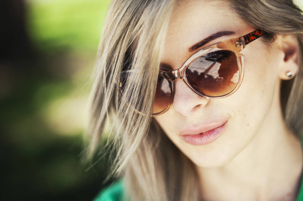 Nahaufnahme Porträt einer schönen Frau mit Sonnenbrille, die tagsüber im Park posiert - Foto, Bild