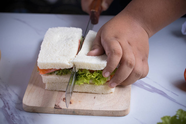 Hands are using a knife to cut the bread sandwiches for breakfast. - Photo, Image