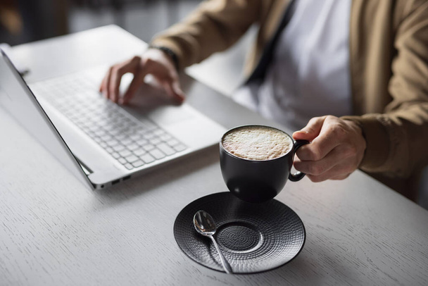Closeup male hands working on laptop keyboard take a cup of latte - Foto, Bild