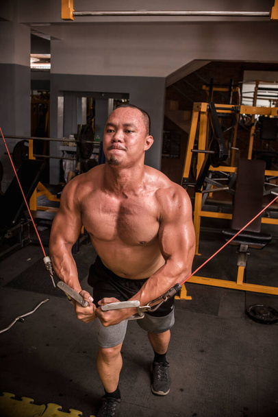 Um homem asiático musculoso aperta seus músculos peitorais e bloqueia os braços enquanto faz cruzamentos de cabos. Exercício torácico intenso. - Foto, Imagem
