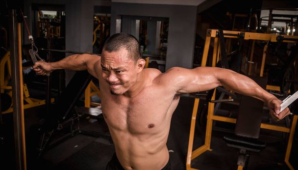 Un hombre asiático musculoso y resistente haciendo un intenso entrenamiento de cruces de cables, programa de día en el pecho. - Foto, Imagen