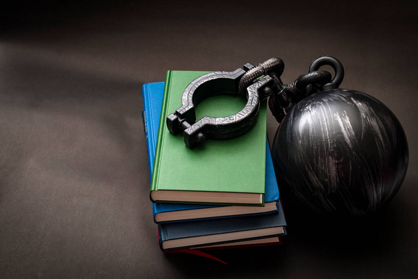 Student debt concept with a stack of books next to a ball and chain symbolizing the burden tuition costs represent with copy space - Photo, Image
