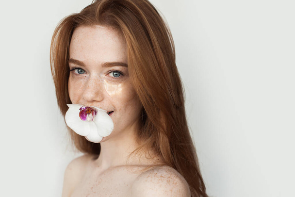 Ginger woman with freckles is smiling at camera holding a flower in her mouth and wearing eye patches - Photo, Image