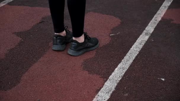 piernas de corredor femenino en zapatillas negras en pista de atletismo, vista trasera de cerca - Imágenes, Vídeo