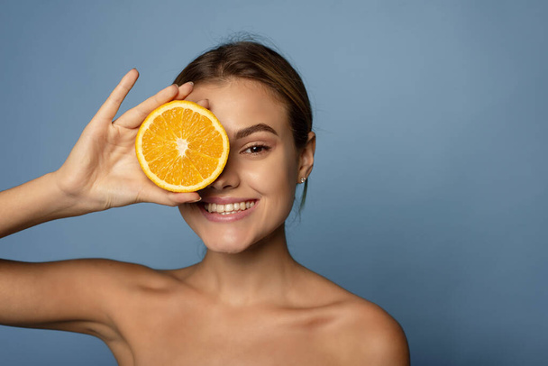 Счастливая молодая женщина держит цитрусовые на лице. Концепция витамина С - Фото, изображение