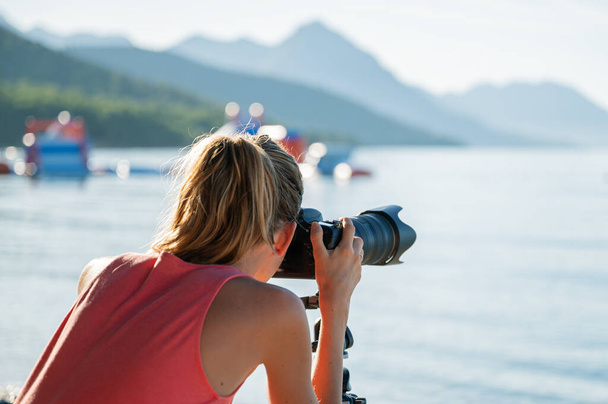 View from behind of a young female photographer taking photos of beautiful sea and landscape in early summer morning. - Photo, Image