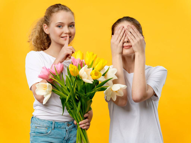 жінка з закритими очима і маленька дівчинка з букетом квітів, що тримає палець біля її губ
 - Фото, зображення