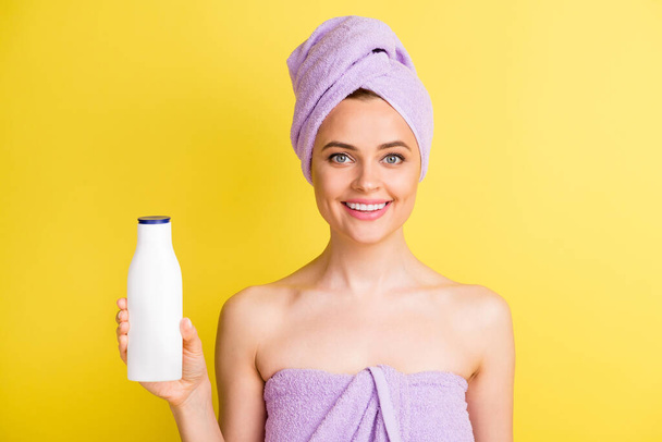 Close-up portrait of lovely cheerful girl holding in hand lotion bottle pure skin isolated over vibrant yellow color background - 写真・画像