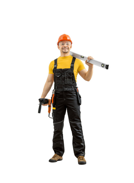 šťastný pracovník opravář nebo stavitel s konstrukčním nástrojem - kladivo vrtačka perforátor a lihoviny, stojí celé tělo v uniformě a úsměv, na bílém pozadí, izolované. Koncept servisu a výstavby oprav - Fotografie, Obrázek
