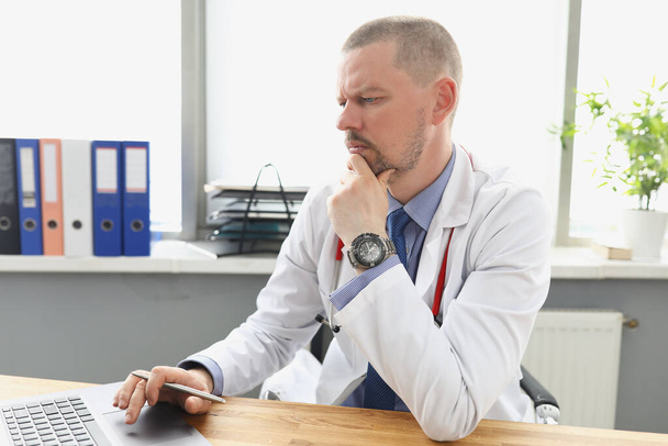 Чоловік лікар дивиться на екран ноутбука в офісі
 - Фото, зображення