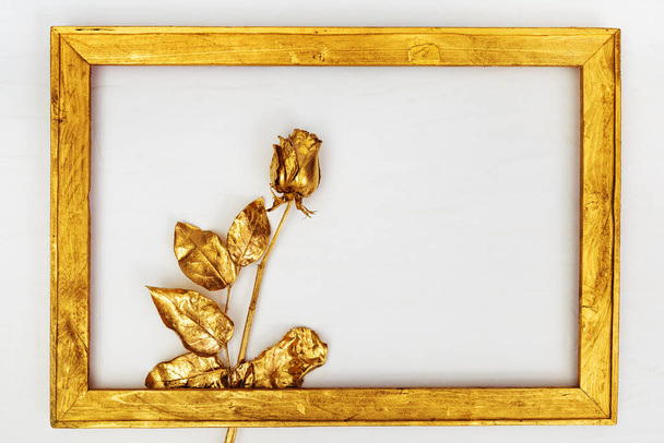 One golden painted rose in wooden frame on white background with copy space. Creative flower. Minimal holiday celebration concept. - Photo, image