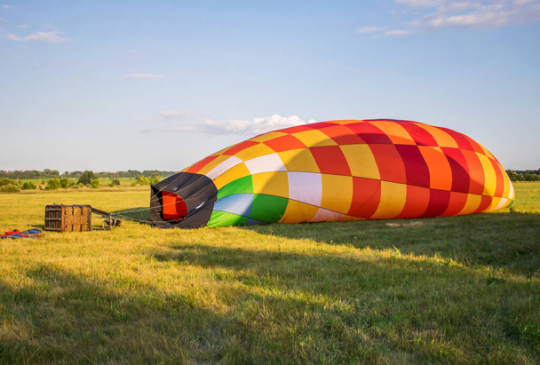 προετοιμασία του αερόστατου για την πτήση. γεμίζοντας την μπάλα με αέριο. φωτεινό, πολύχρωμο αερόστατο θερμού αέρα στο έδαφος το καλοκαίρι  - Φωτογραφία, εικόνα