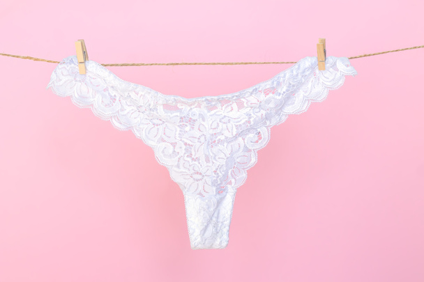 Female white sexy lace panties hanging on clothesline on pink background - Photo, Image
