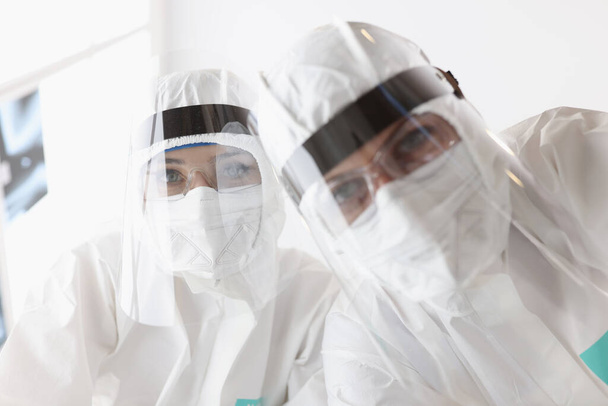 Médicos en trajes de protección contra la peste y pantallas mirando al paciente - Foto, Imagen