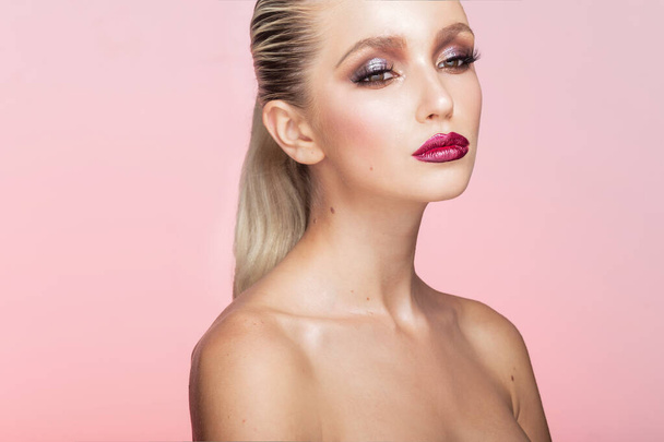 Gros plan portrait de belle jeune femme avec un maquillage parfait et les cheveux lissés posant en studio, fond rose isolé. - Photo, image