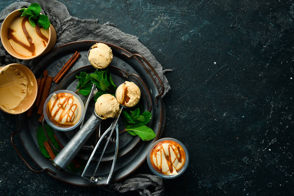 Caramel ice cream with mint and salted caramel. Ice cream spoon. On a black stone background, top view. - Foto, imagen