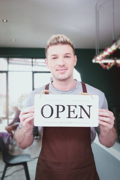 Store owner man holding open sign broad at entrance door of restaurant and coffee shop for telling customers that shop is ready to service. - 写真・画像