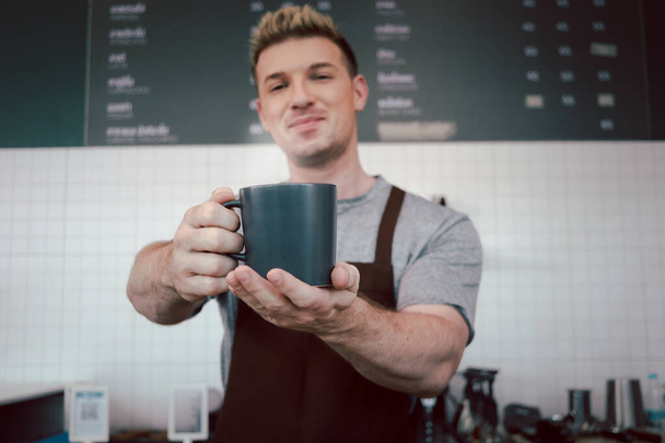 Zbliżenie baristycznych rąk trzymających filiżankę gorącej kawy w kawiarni, obsługa kelnerska podająca kawę klientowi w kawiarni lady bar. - Zdjęcie, obraz
