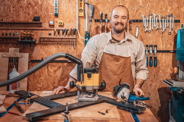 portrait of a smiling caucasian carpenter with apron in his workshop - Фото, изображение