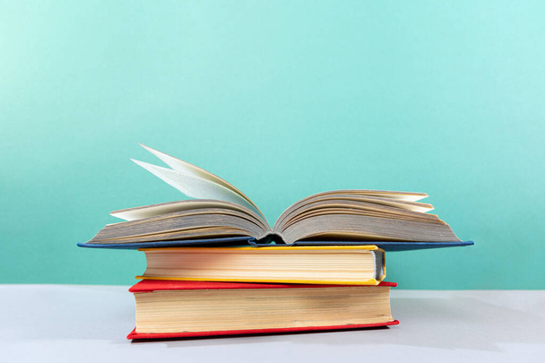 Könyv Világnap. Van egy halom könyv az asztalon, egy nyitott könyvvel a tetején. Türkiz háttér. Az oktatás és az olvasás fogalma. - Fotó, kép