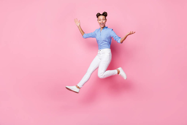 Фотография в полный рост прыгающей сумасшедшей девушки в повседневной одежде, смеющейся на фоне розового цвета - Фото, изображение