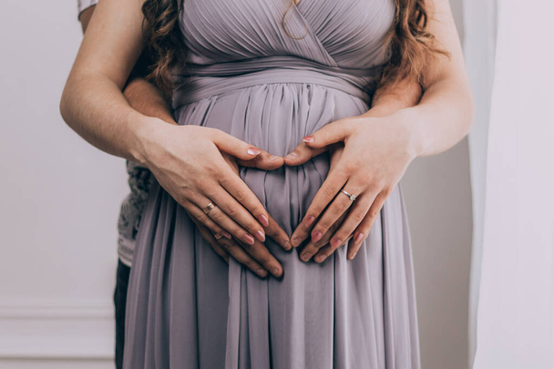 Elbiseli hamile bir kız ellerini karnına koyuyor.  - Fotoğraf, Görsel