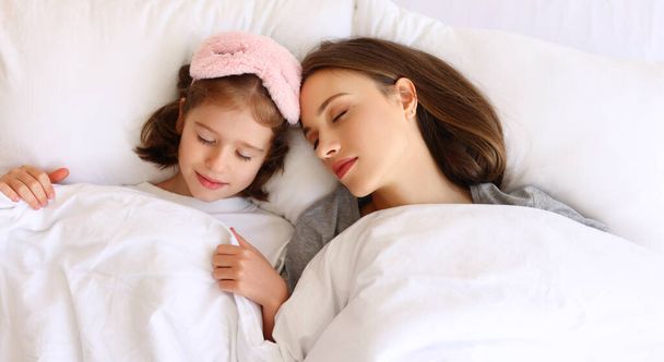 Fentről fiatal anya és lánya feküdt az ágyon paplan alatt, és alszik reggel otthon - Fotó, kép
