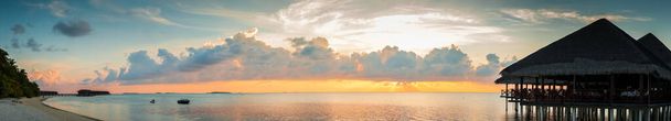 モルディブ島の夕日、豪華なウォーターヴィラリゾートと木製の桟橋。夏休みの休暇と旅行のコンセプトのための美しい空と雲とビーチの背景。パノラマビュー - 写真・画像