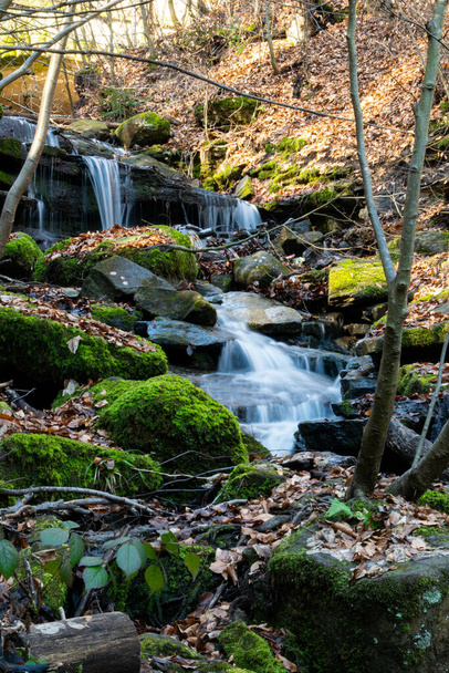 A vertical shot of a small waterfall cascading over the mossy rocks - Foto, afbeelding