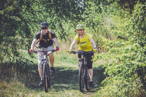 Young couple racing on mountain bikes on country road - Фото, зображення