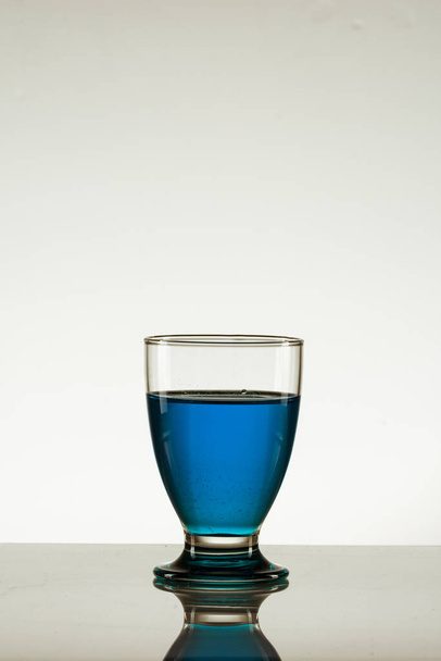 反射面に隔離された青い飲み物のガラスの垂直ショット - 写真・画像