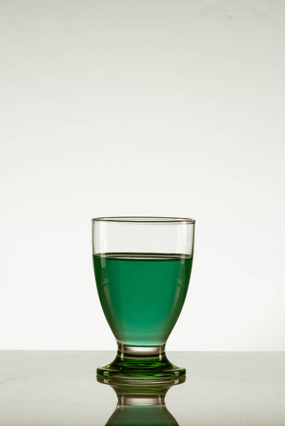 A vertical shot of a glass of green drink isolated on a reflective surface - Foto, Imagem