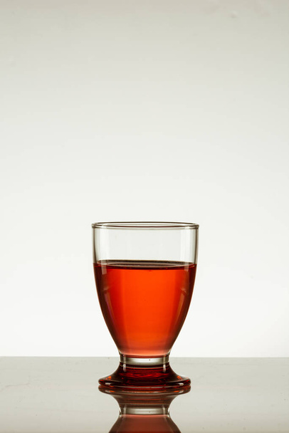 A vertical shot of a glass of red drink isolated on a reflective surface - Fotó, kép