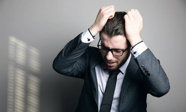 a man in a suit and glasses tears his hair on a gray background - Foto, immagini
