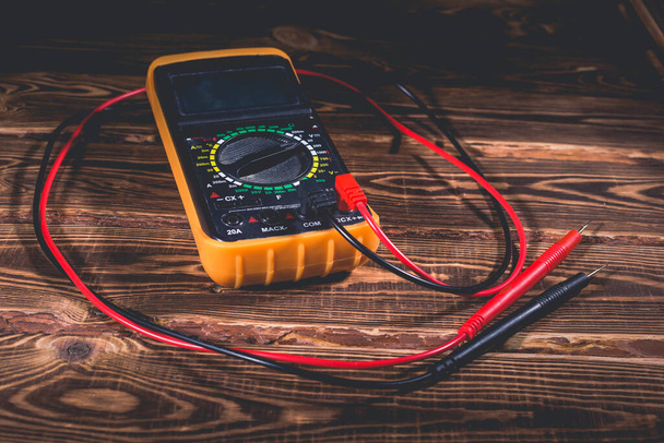 Multimeter and two test leads on a wooden background. A studio photo with hard lighting. - Photo, Image