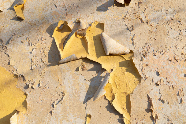 Pelyhes festék réteg közelről. Átvészelt durva textúra a régi fal sárga pehely festék pasztell színű kő felületén. Napsütéses nap. Javítási és újjáépítési koncepció  - Fotó, kép