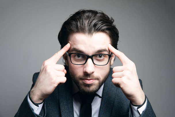 a man in a suit and glasses put his fingers on his temples on a gray background - Foto, imagen