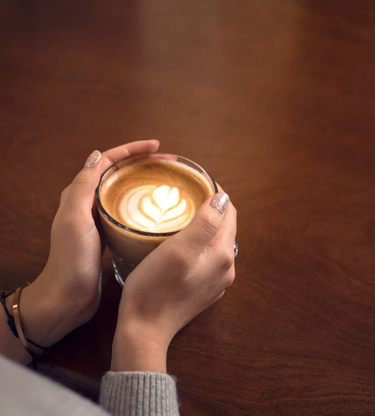 Kávé tejjel egy magas pohárban. kávé a fa asztalon. kőfal. vintage belső tér. A nő egy csésze kávét tart a kezében. A fiatal lány kávét iszik. csésze a fa asztalon. fénykép.  - Fotó, kép