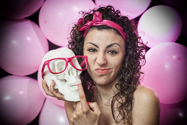 божевільна дівчина тримає білий череп з рожевими окулярами, на рожевому фоні
  - Фото, зображення