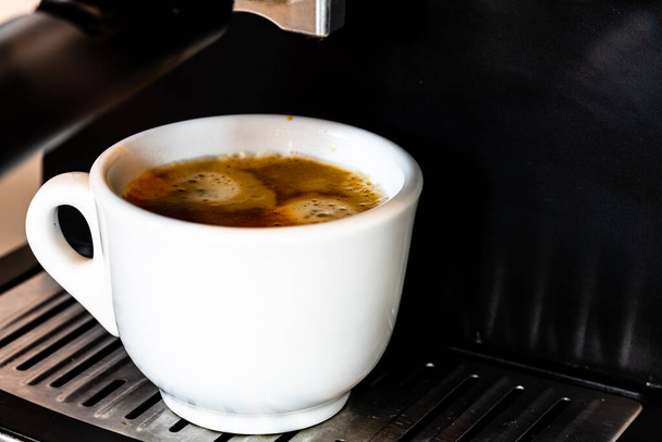 Egy csésze eszpresszó, miközben a csésze egy kávéfőzőt tölt ki. - Fotó, kép