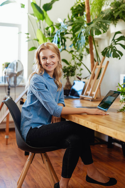 Aantrekkelijke en vrolijke vrouwelijke kantoormedewerker zit aan tafel met een laptop - Foto, afbeelding
