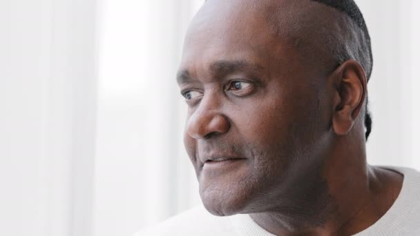 Mies muotokuva vanha keski-ikäinen aikuinen 50s afrikkalainen amerikkalainen mies katselee ulos ikkunasta kotona ajattelu haaveilee harkitsee, lähikuva vanhukset kypsä mietteliäs isä isoisä katsoo pois suunnittelu odottaa - Materiaali, video
