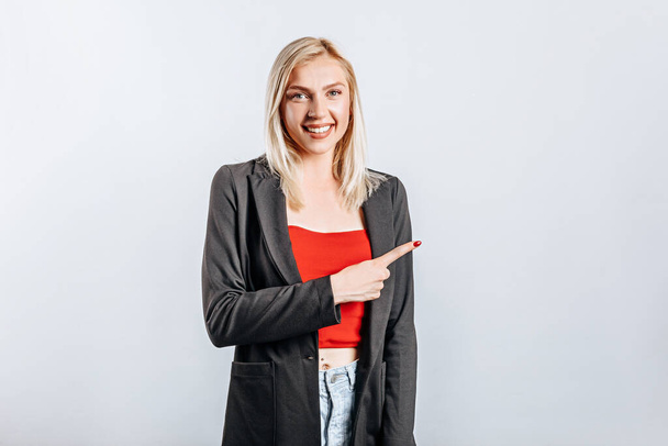 Portrait of a smiling girl pointing finger up at copyspace isolated on a white background. A woman points to an idea, a place for advertising. Positive blonde. - Photo, Image