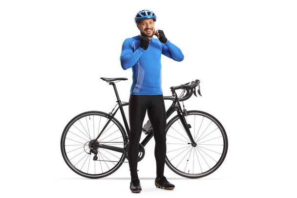 Full length portrait of a male cyclist putting on a helmet and smiling next to his bicycle isolated on white background - Zdjęcie, obraz
