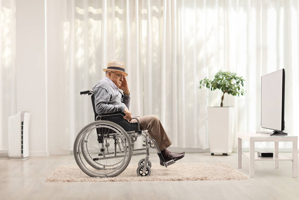 Unhappy elderly man in a wheelchair sitting at home in front of a tv - Foto, afbeelding