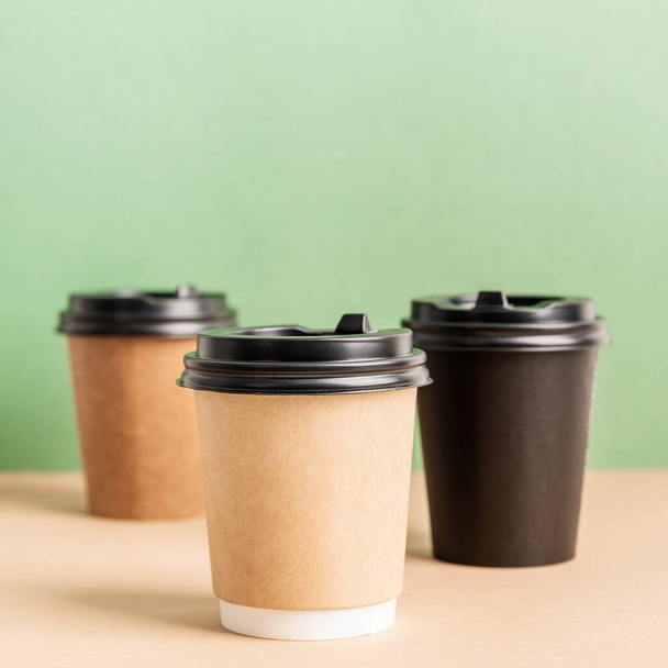Umweltfreundliches Einweggeschirr ohne Abfall. Schwarze Kaffeetassen zum Mitnehmen aus Papier auf grünem und braunem Hintergrund - Foto, Bild