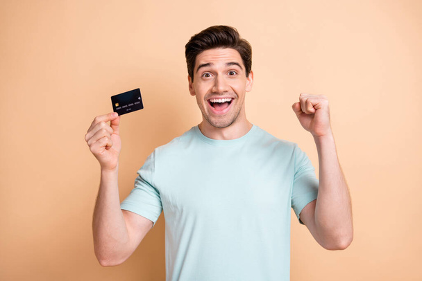 Portrait of nice cheerful guy holding in hand bank card celebrating loan deposit success isolated over beige pastel color background - Photo, Image