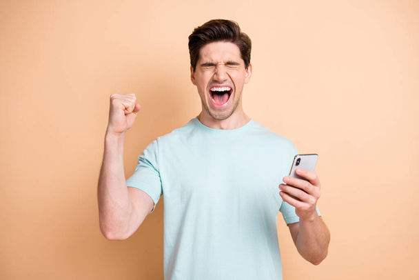 Portrait of nice cheerful overjoyed guy influenzer using device having fun rejoicing smm isolated over beige pastel color background - Foto, Bild