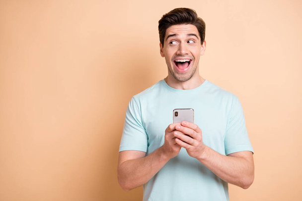 Portrait of nice cheerful amazed guy blogger using gadget looking aside copy space advert isolated over beige pastel color background - Fotó, kép